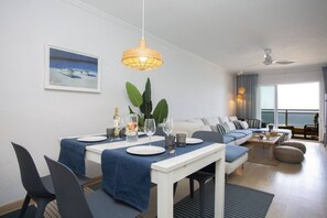 A dining area with a table set for four, a sofa, a balcony, and a ceiling fan.