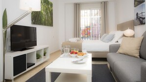 A modern hotel room with a flat-screen TV, a dining table with breakfast, a sofa, and a large window with curtains.