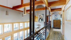 Un intérieur spacieux avec de hauts plafonds, des poutres apparentes et de grandes fenêtres offrant une vue sur l’extérieur.