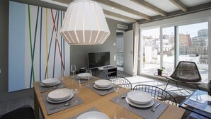 Un coin repas avec une table en bois dressée pour quatre personnes, un téléviseur et une grande fenêtre donnant sur la ville.