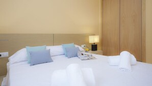 A hotel room with a bed, pillows, a nightstand with a lamp, and a wooden wardrobe. - SingularStays Moncofar Beach (Moncofar)