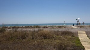 A beach with a lifeguard tower, a wooden walkway, and a clear blue sky. - SingularStays Moncofar Beach (Moncofar)