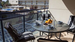 A round glass table with four chairs, a bowl of fruit, and a glass of water on a balcony with a pool view. - SingularStays Moncofar Beach (Moncofar)