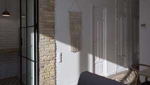 A room with a brick wall, white doors, a hanging macrame wall hanging, and a wooden chair. - SingularStays Parque Central XIV (Valencia)