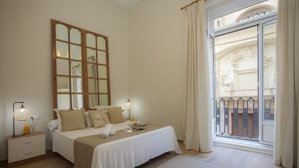 A bedroom with a large bed, a nightstand, a lamp, and a view of a balcony. - SingularStays Seu VI (València)
