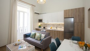 A modern kitchen with white cabinets, a stainless steel refrigerator, and a microwave. There's a dining area with a table and chairs, and a sofa with cushions. - SingularStays Seu VI (València)