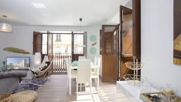 Un salon moderne avec un canapé, une table à manger et des chaises. Il y a un balcon avec vue sur les immeubles.