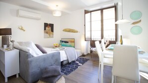 A modern living room with a sofa, a dining table with chairs, a large window with a view, and decorative wall art. - SingularStays Valencia Center III (València)