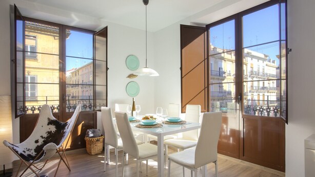 A dining area with a table set for four, large windows, and a view of buildings outside. - SingularStays Valencia Center III (València)