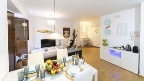Eine moderne Küche mit weißen Schränken, ein Essbereich mit Tisch für vier Personen und eine Wohnfläche mit Fernseher und Sitzgelegenheiten.