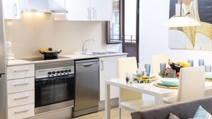 Eine kompakte Küche mit Herd, Backofen und Geschirrspüler, ein Essbereich mit Tisch und Stühlen und ein großes Fenster, das für natürliches Licht sorgt.
