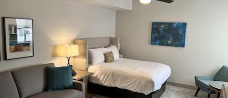 Habitación de hotel con cama, escritorio, sillón, sofá, ventilador de techo y obras de arte en las paredes.