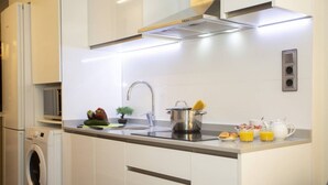 A modern kitchen with a built-in washing machine, a sink, a stove, and a breakfast setup with orange juice and eggs.