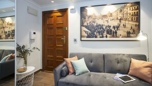 A modern hotel lobby with a grey sofa, a wooden door, and a large historical photograph on the wall.