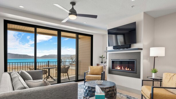 Ein modernes Wohnzimmer mit Kamin, Flachbildfernseher und Balkon mit Seeblick.