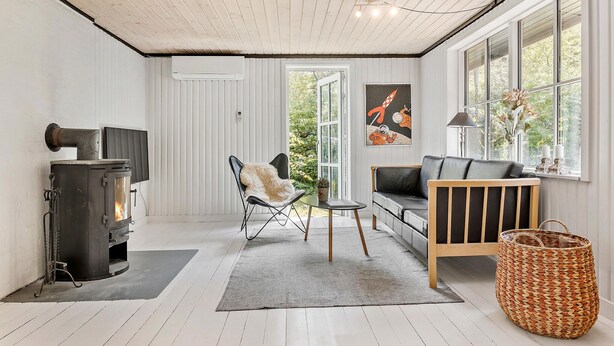 Ein gemütliches Zimmer mit Kaminofen, einer bequemen Couch, einem Sessel und einem großen Fenster.