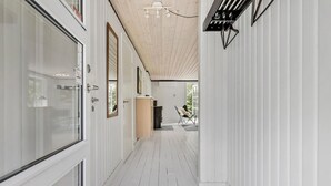 Ein schmaler Korridor mit weißen Wänden und Holzböden, der zu einem Raum mit einem großen Fenster und einem Sessel führt.