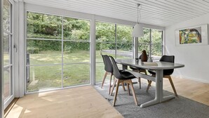 Ein moderner Essbereich mit einer großen Schiebeglastür, die zu einem Garten führt, einem Tisch mit Stühlen und einer hängenden Leuchte.
