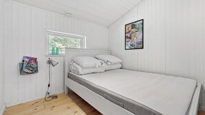 Ein heller Raum mit einem Bett, einem Fenster, einer Wandlampe und einem gerahmten Bild.