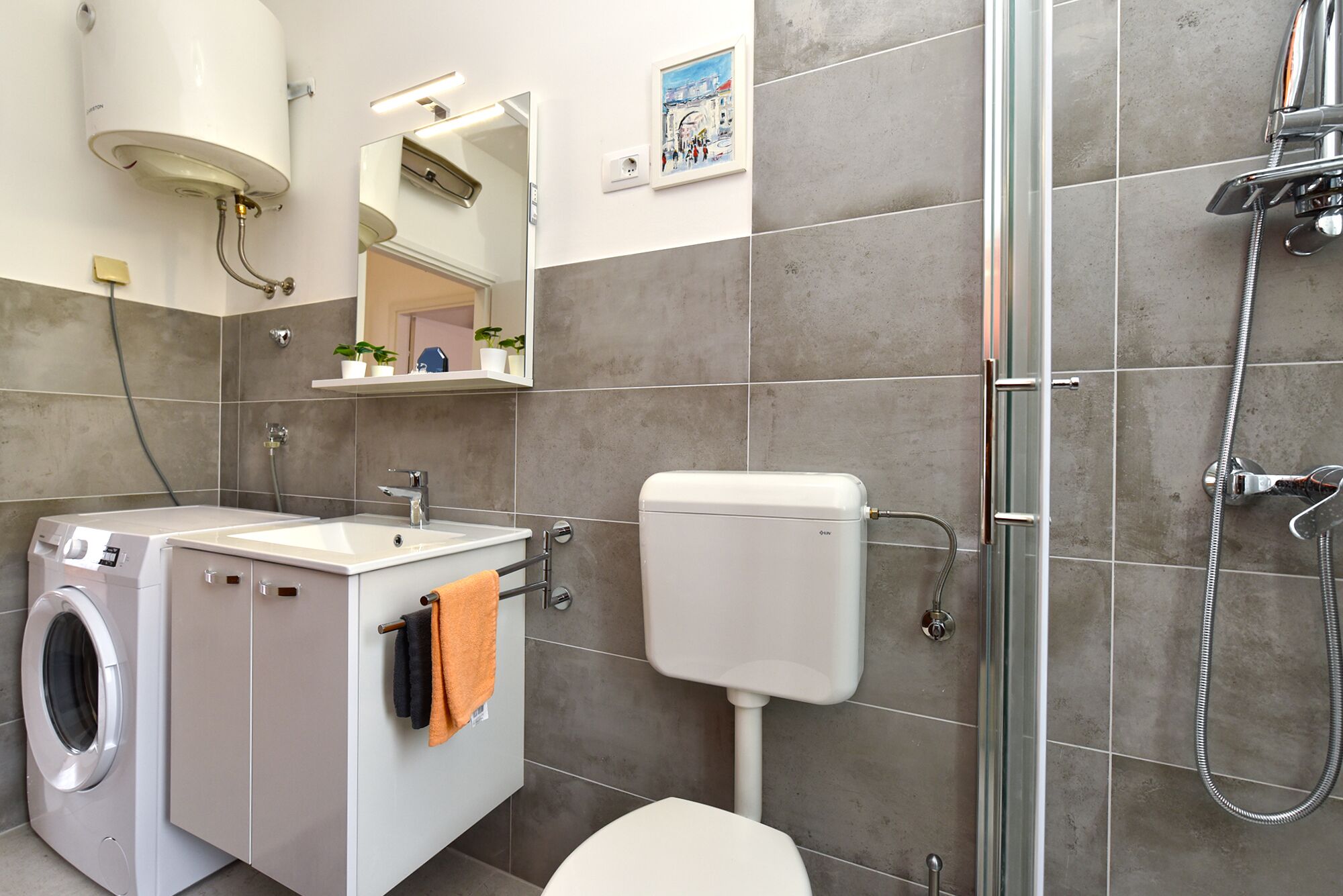 Une salle de bain moderne équipée d’un lave-linge, d’un évier, de toilettes et d’une douche.
