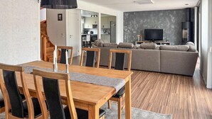 A modern living room with a dining area, grey sofa, wooden dining table, and a TV. - 3 bedroom beautiful home in Gislaved (Gislaved)