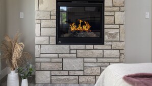 A modern living room with a stone fireplace, a mounted TV displaying "NETFLIX," and a cozy bed in the foreground.