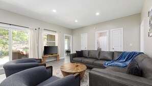 Una sala de estar moderna con un sofá gris, dos sillones, una mesa de centro de madera y un televisor sobre un mueble.