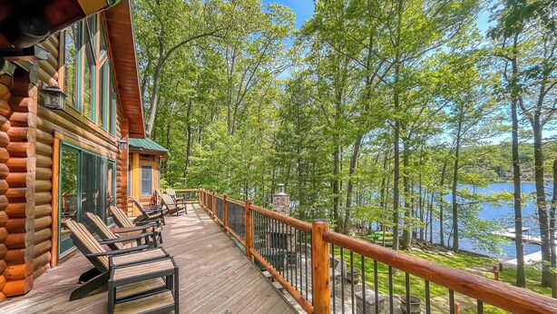 Una terraza de madera con mobiliario exterior y vistas a un lago rodeado de árboles.