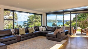 A modern living room with a large sectional sofa, a patterned rug, and large windows offering a view of a lake and greenery.