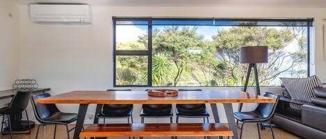 A modern dining area with a wooden table, black chairs, and a large window with a view of trees.