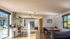 A modern kitchen with a dining area, large windows, and a sofa.