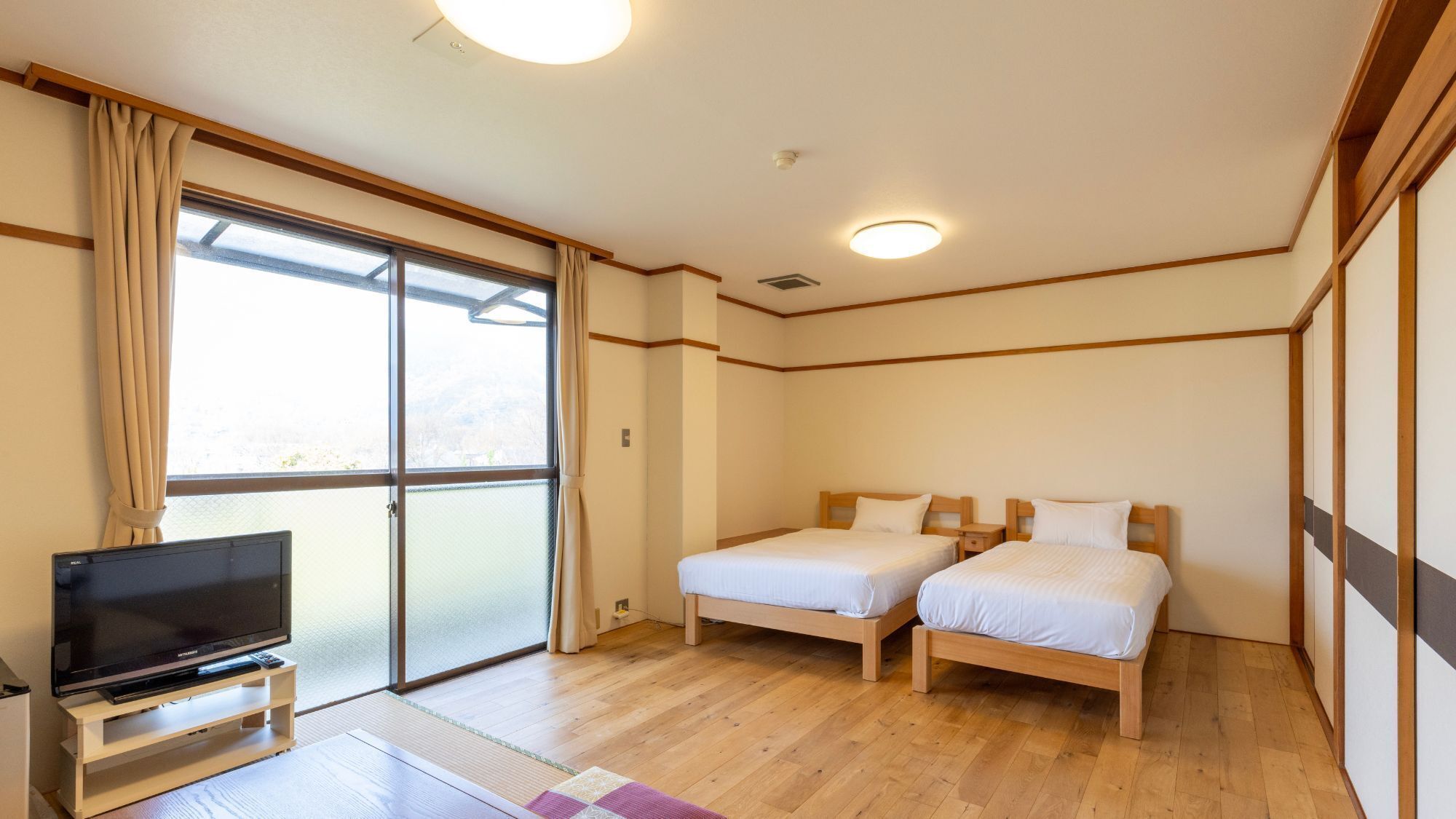 Habitación de hotel con dos camas, televisión y un amplio ventanal corredero.