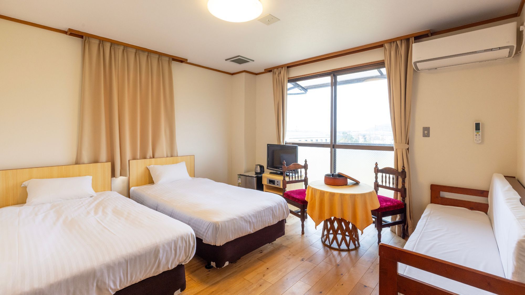 Une chambre d’hôtel avec deux lits, une télévision, une petite table et une fenêtre avec des rideaux.