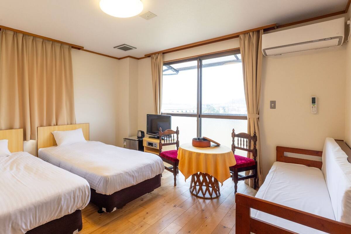 Habitación de hotel con dos camas, televisión, una mesita y ventana con cortinas.