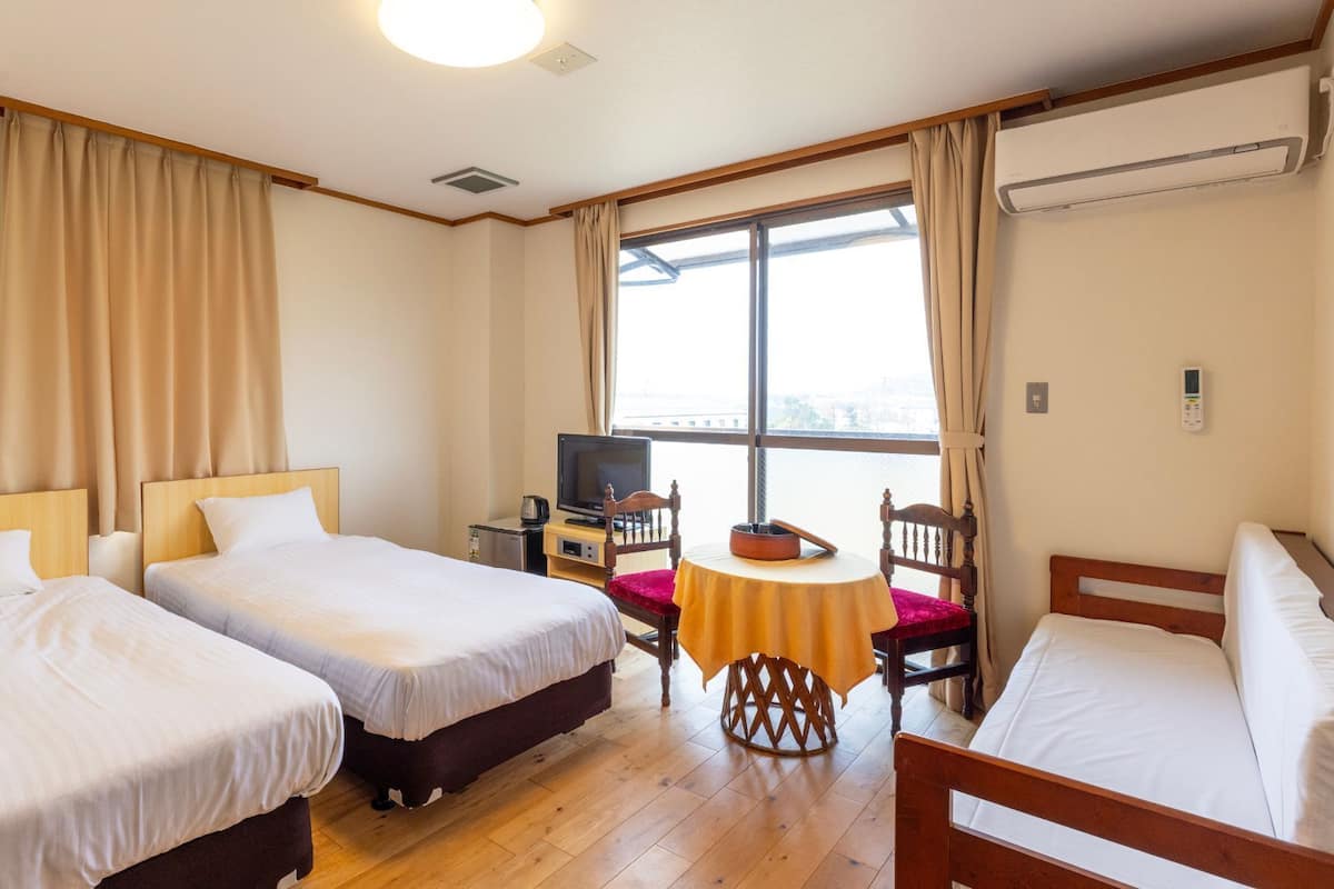 Habitación de hotel con dos camas, televisión, una mesita y ventana con cortinas.