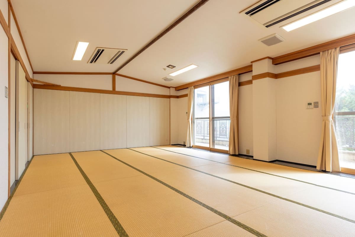 Una habitación con suelo de tatami, puertas correderas, un balcón y rejillas en el techo.