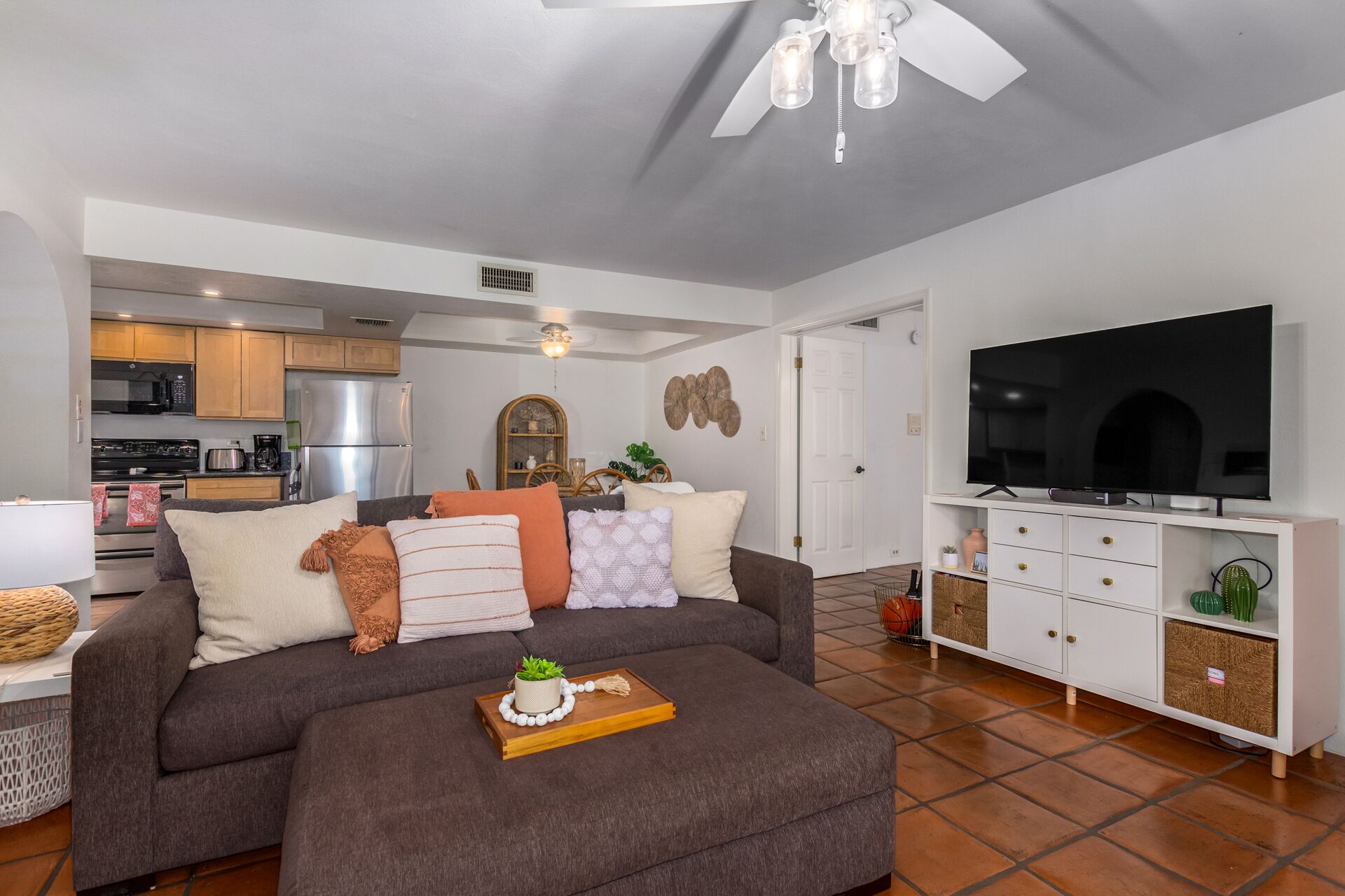 A modern living room with a grey sofa, a wooden coffee table, and a flat-screen TV on a white cabinet.