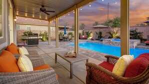 An outdoor patio area with a pool, wicker furniture, and a barbecue grill.