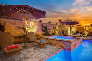Un área junto a la piscina con sillones de descanso, sombrillas y una pared de ladrillo.
