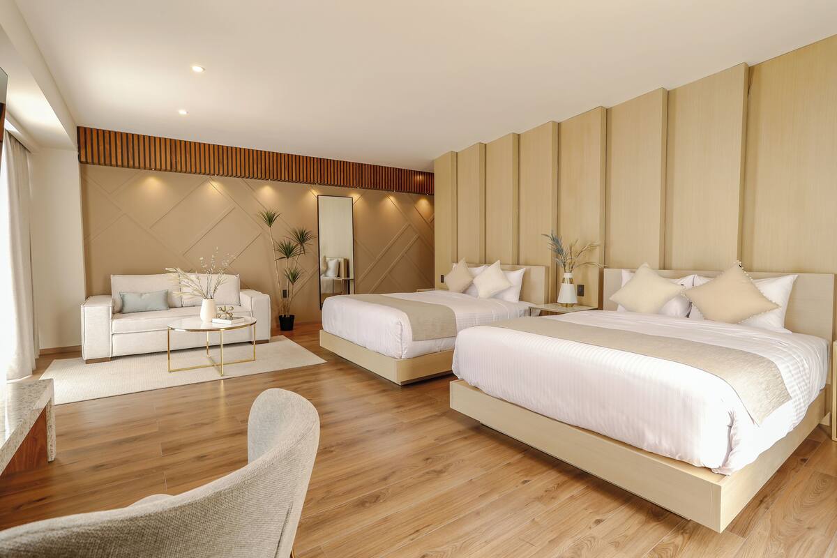 A modern hotel room with two beds, a sofa, a coffee table, and a large mirror.