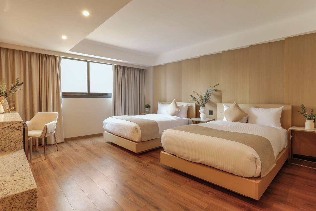 A modern hotel room with two beds, a desk, and a chair.