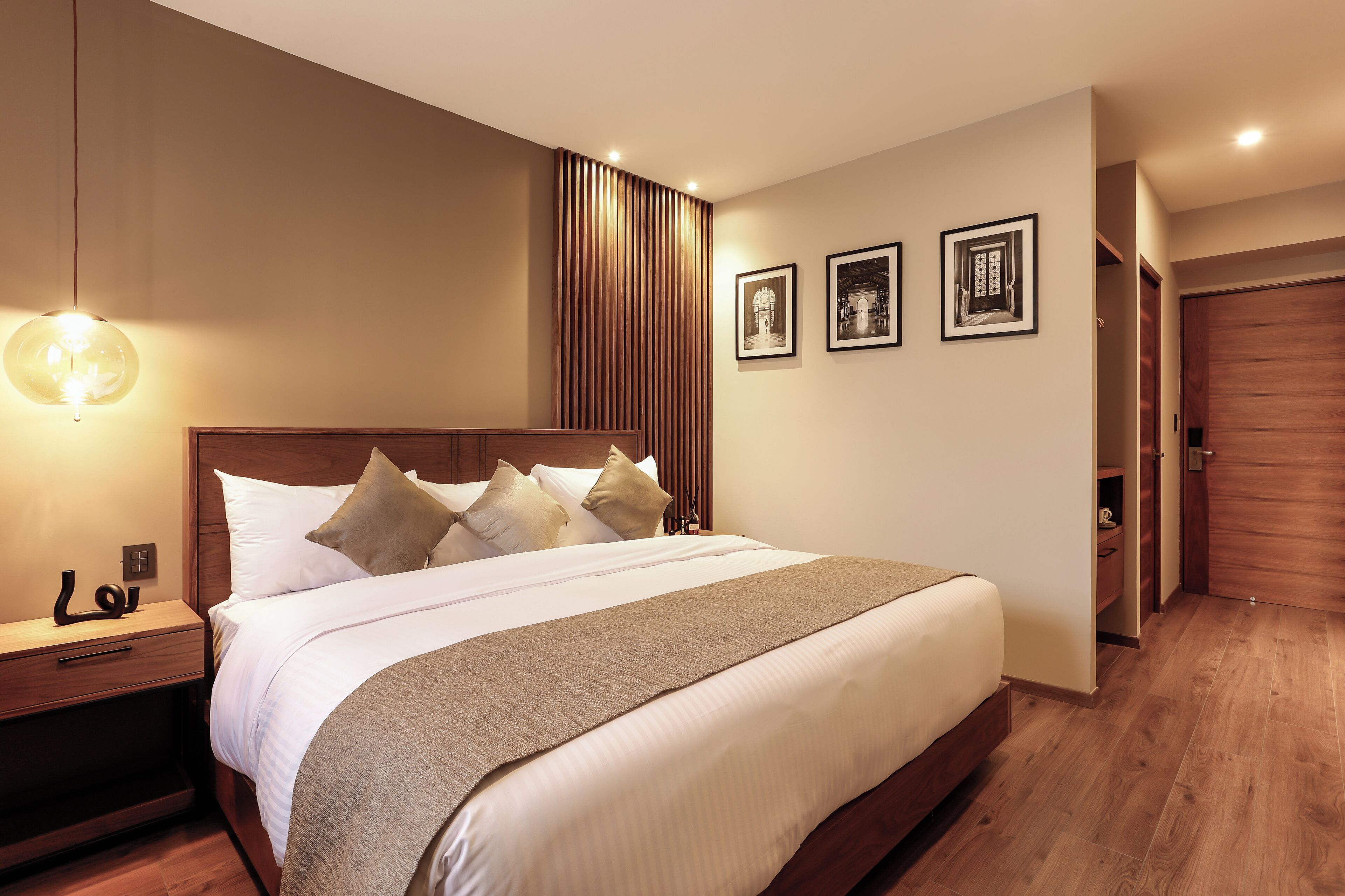 A neatly made bed with a wooden headboard, a bedside table with a lamp, and three framed pictures on the wall.