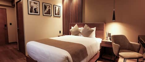 Habitación de hotel con una cama grande, un escritorio con silla y una lámpara de pared.