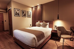 Une chambre d’hôtel avec un grand lit, un bureau avec une chaise et une lampe fixée au mur.