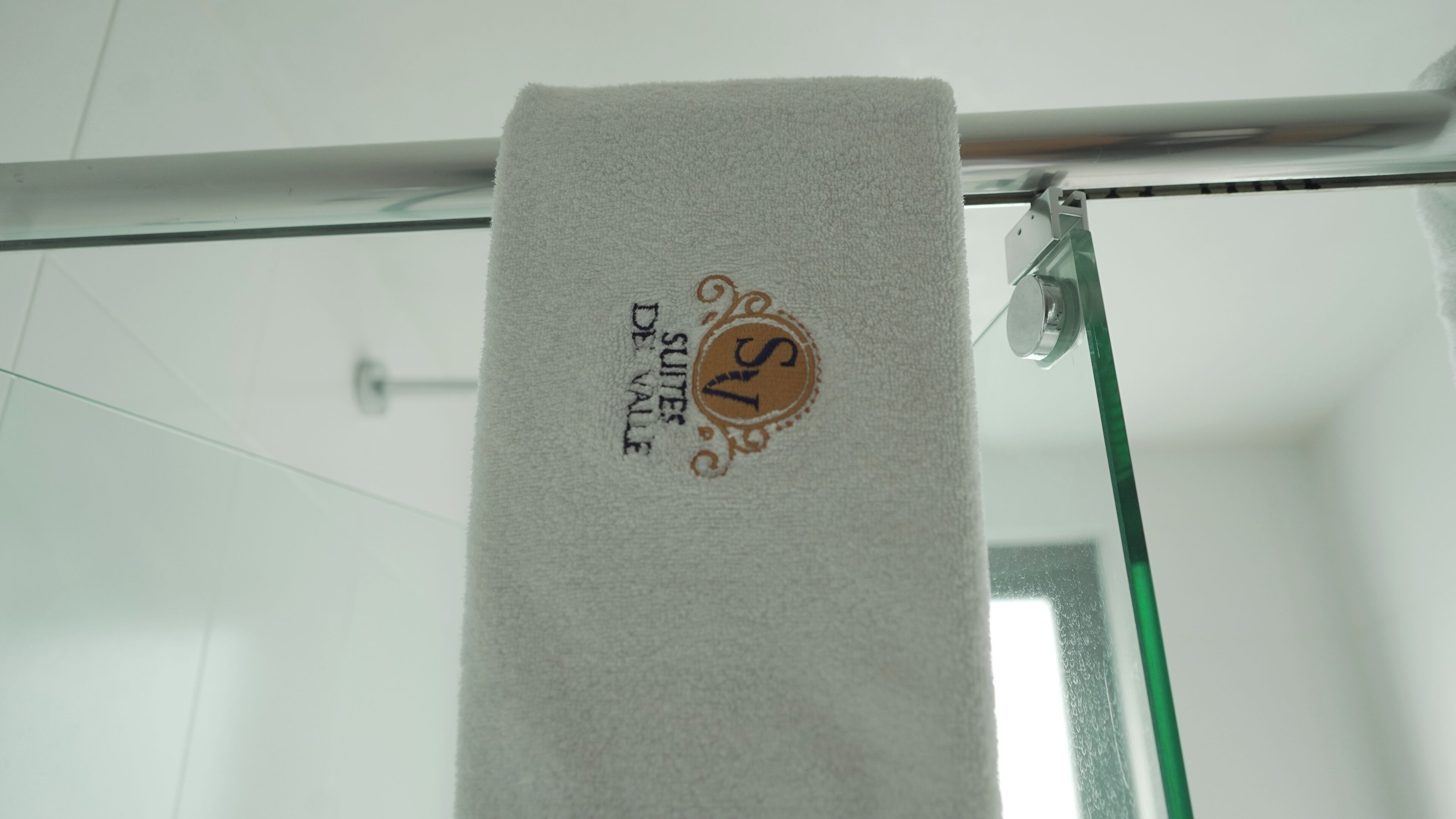 Una toalla blanca colgada en una barra de ducha de vidrio con un logotipo y texto que indican que es de una suite de hotel.