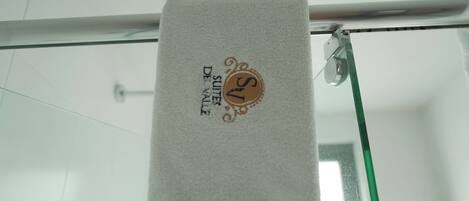 Una toalla blanca colgada en una barra de ducha de vidrio con un logotipo y texto que indican que es de una suite de hotel.