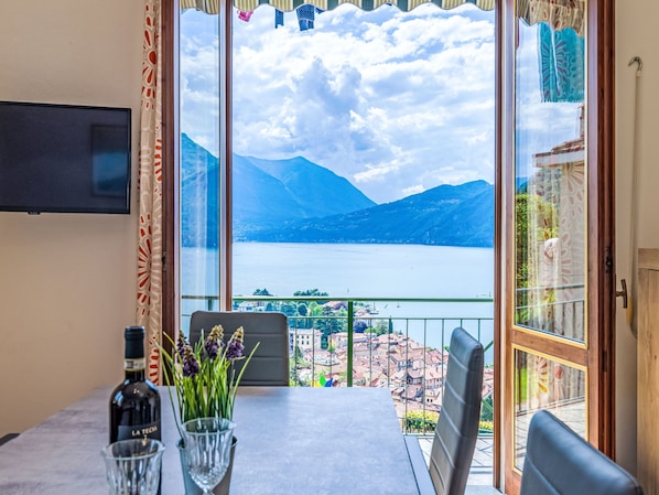 A dining area with a table, chairs, a bottle of wine, and a glass. A window offers a view of a lake and mountains.