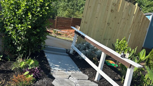 Ein Gartenpfad mit trittfesten Steinen, umgeben von Pflanzen und einem Holzzaun.
