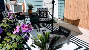 Ein Terrassenbereich mit einem gestreiften Outdoor-Teppich, einem Tisch mit Stühlen und einem Topfpflanzen.