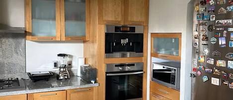 A modern kitchen with wooden cabinets, a built-in oven, a microwave, and a refrigerator adorned with magnets.